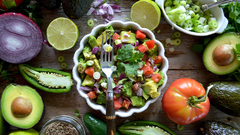Bowl of assorted vegetables on a wooden table surrounded by whole veggies