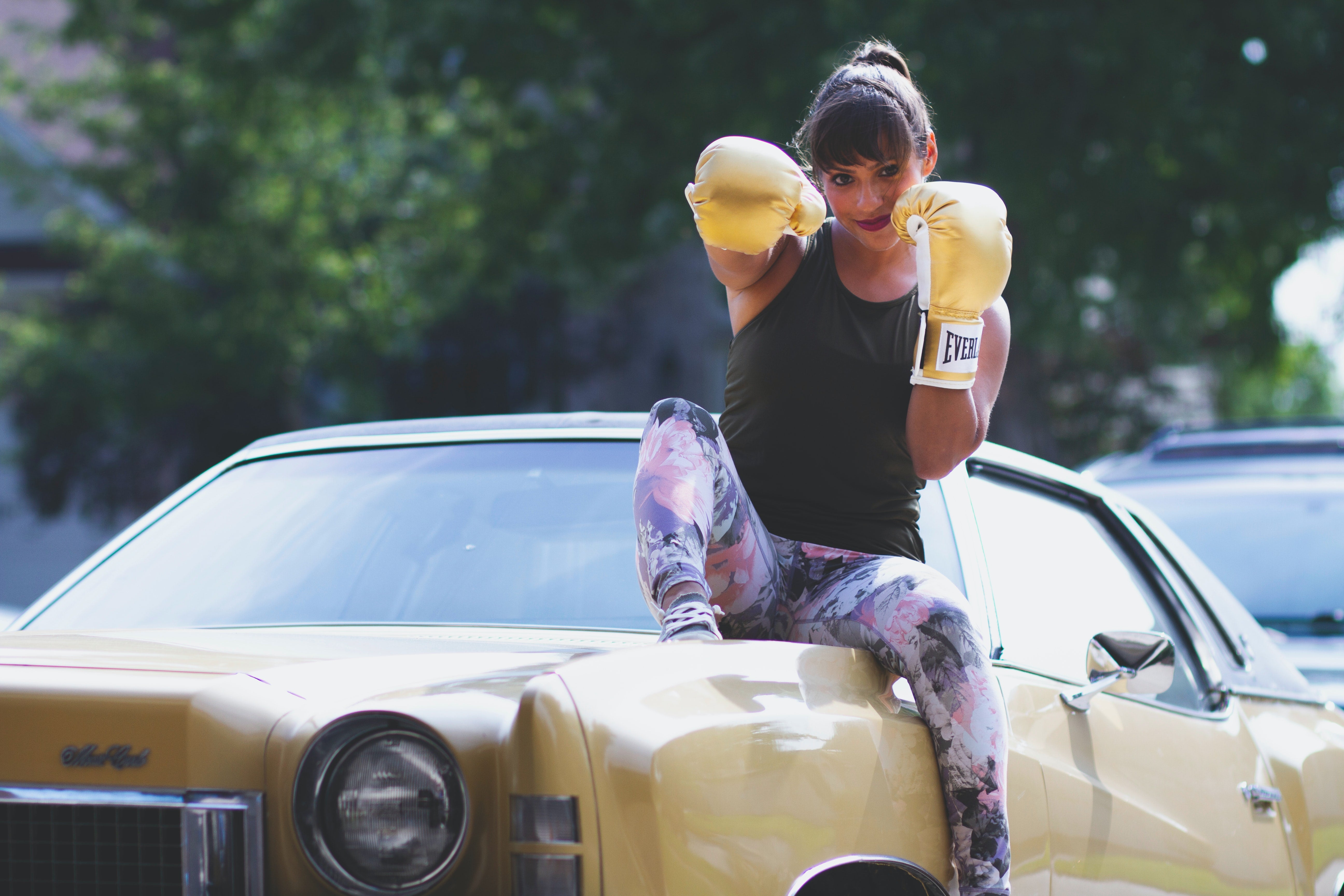 Woman wearing yellow boxing gloves on top of a vintage yellow car